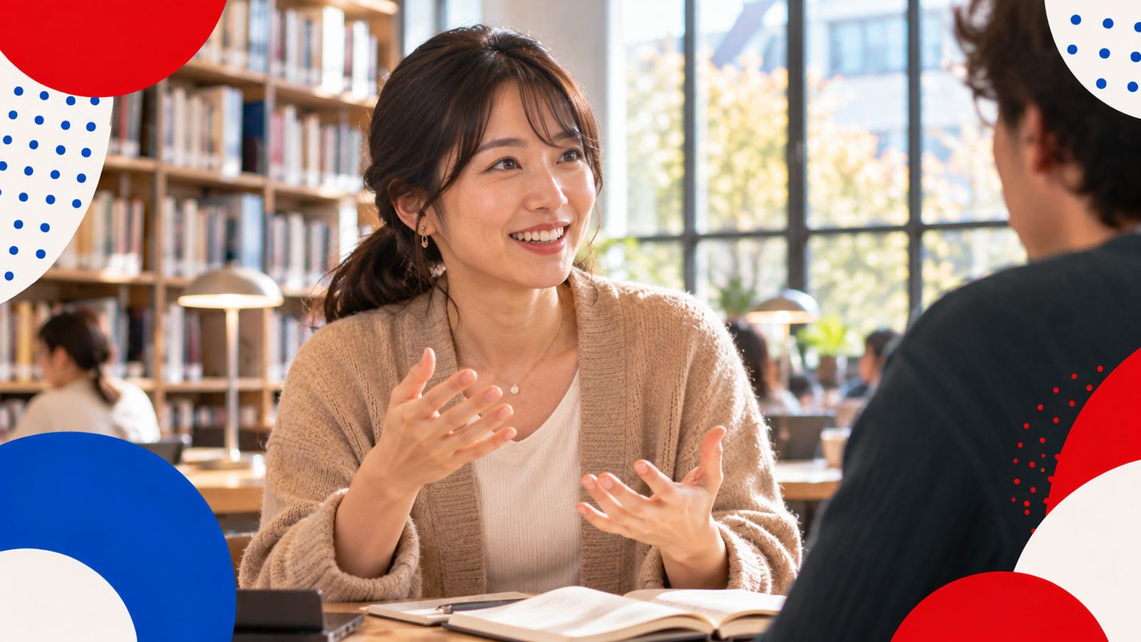 図書館の窓辺で、身ぶりをまじえて笑顔で説明する日本人の女性