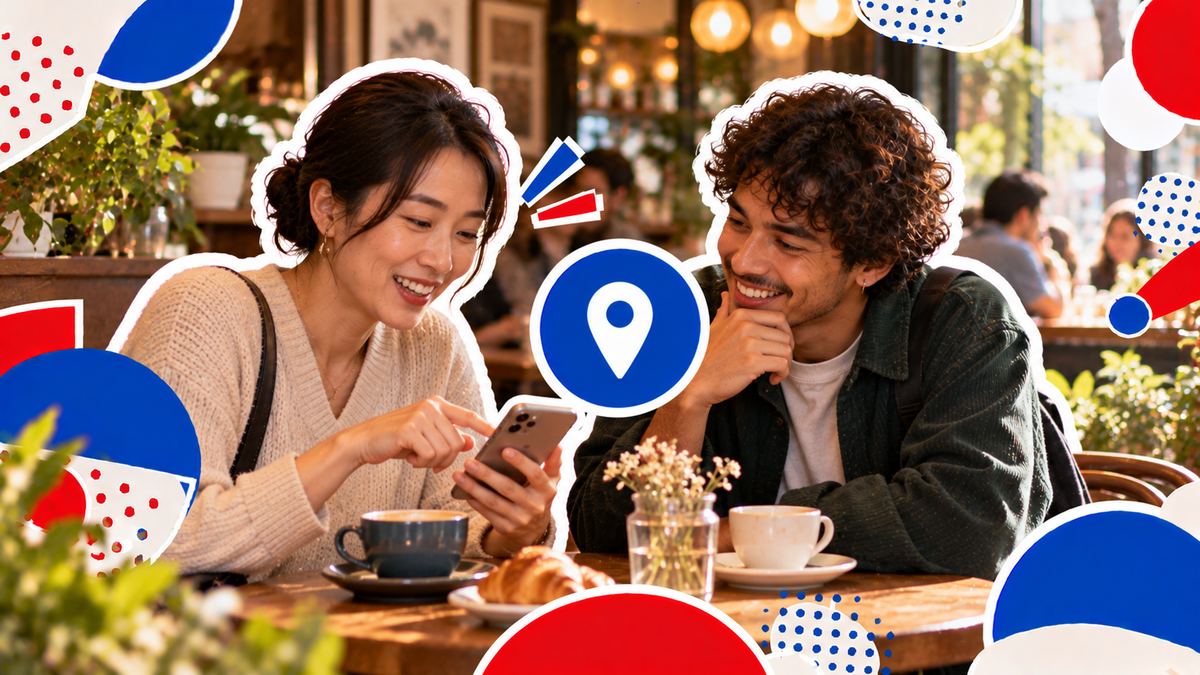 Two people at a café table, one showing a place on her phone while the other leans in and smiles